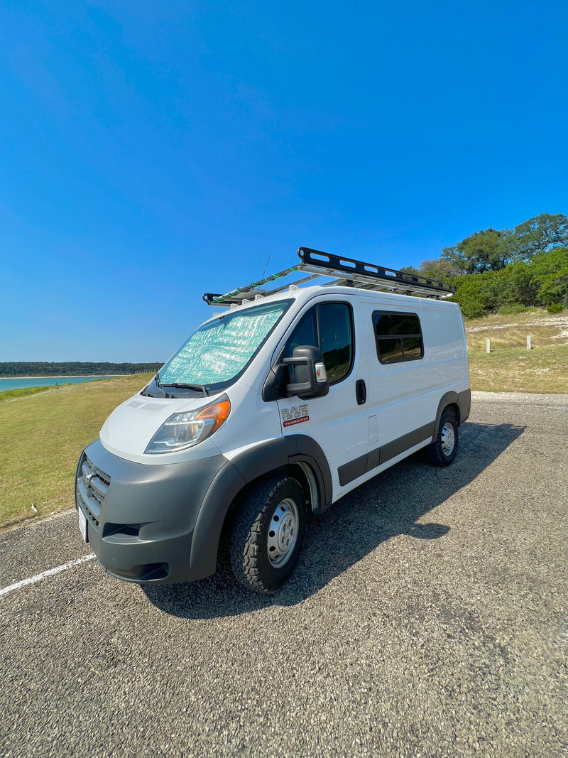 White Ram ProMaster rv rental van with roof rack, parked by a lake under a clear sky. Sunshade on windshield. — photo 16