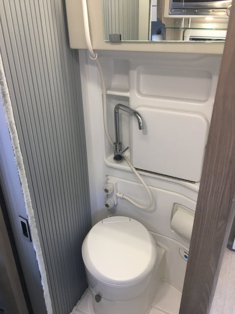 This **rv rental** compact wet bath features a toilet, pull-out faucet/shower, mirror, and ribbed walls for functional amenities.