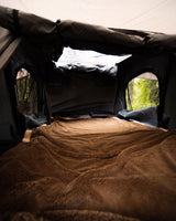 Cozy RV rental sleeping area with a plush brown blanket and forest views. Perfect for outdoor adventures and camping!