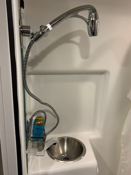 Compact wet bath setup in an RV rental, featuring a handheld shower, small sink, and amenity caddy.