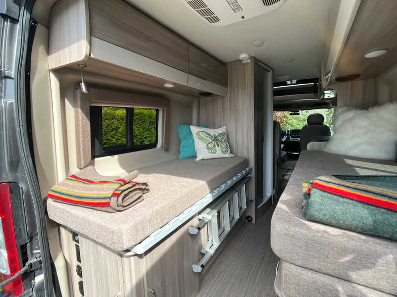 Compact RV rental interior featuring cozy beds, overhead storage, and a scenic window view, ideal for travel. — photo 3