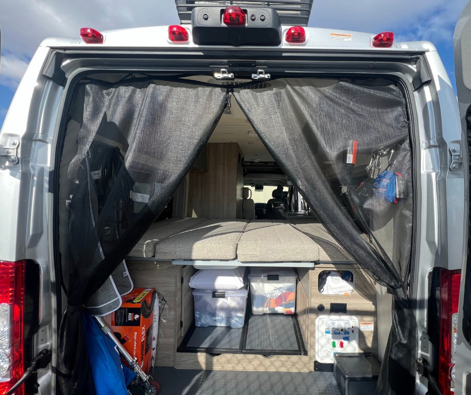 Inside an RV rental: rear view shows a mesh bug screen, modular bed, storage, and utility panel.
