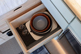 RV rental kitchen drawer open, showing organized plates, bowls, glasses, and a cutting board on a non-slip mat.