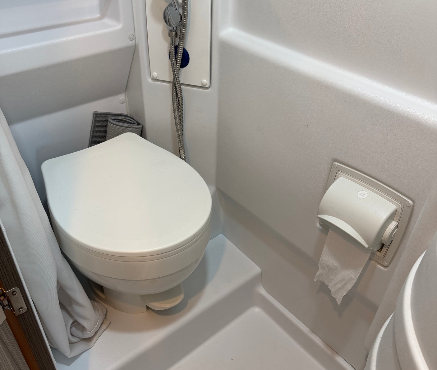 Compact RV rental bathroom featuring a white toilet with a foot flush, shower head, and toilet paper roll.