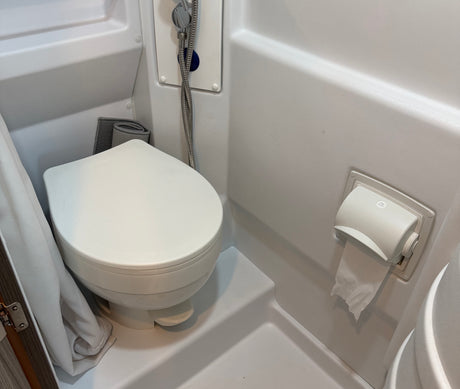 Compact RV rental bathroom featuring a white toilet with a foot flush, shower head, and toilet paper roll.