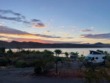 Stunning sunset at a lakeside campground with an RV rental. Mountains frame the scenic view of the water and sky.