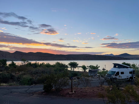 Stunning sunset at a lakeside campground with an RV rental. Mountains frame the scenic view of the water and sky.
