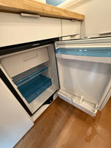 RV rental: Open, empty compact refrigerator with small freezer, blue shelves, and water on the wood floor.