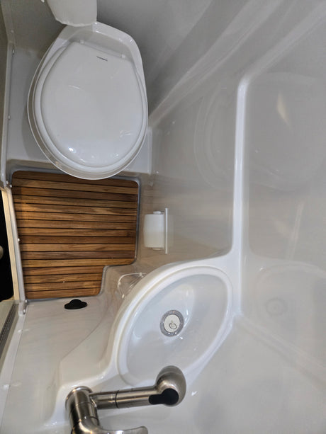 Compact RV rental bathroom featuring a Dometic toilet, integrated sink, and shower area with wood slats for drainage.