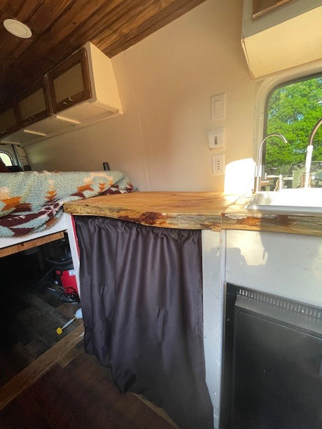Step inside this RV rental! Features a rustic wood ceiling, compact kitchen with sink, comfy bed, and clever storage.