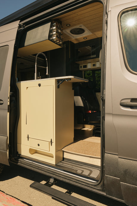 RV rental: A well-equipped camper van interior featuring a kitchenette with sink, spice rack, microwave, and fold-down table.