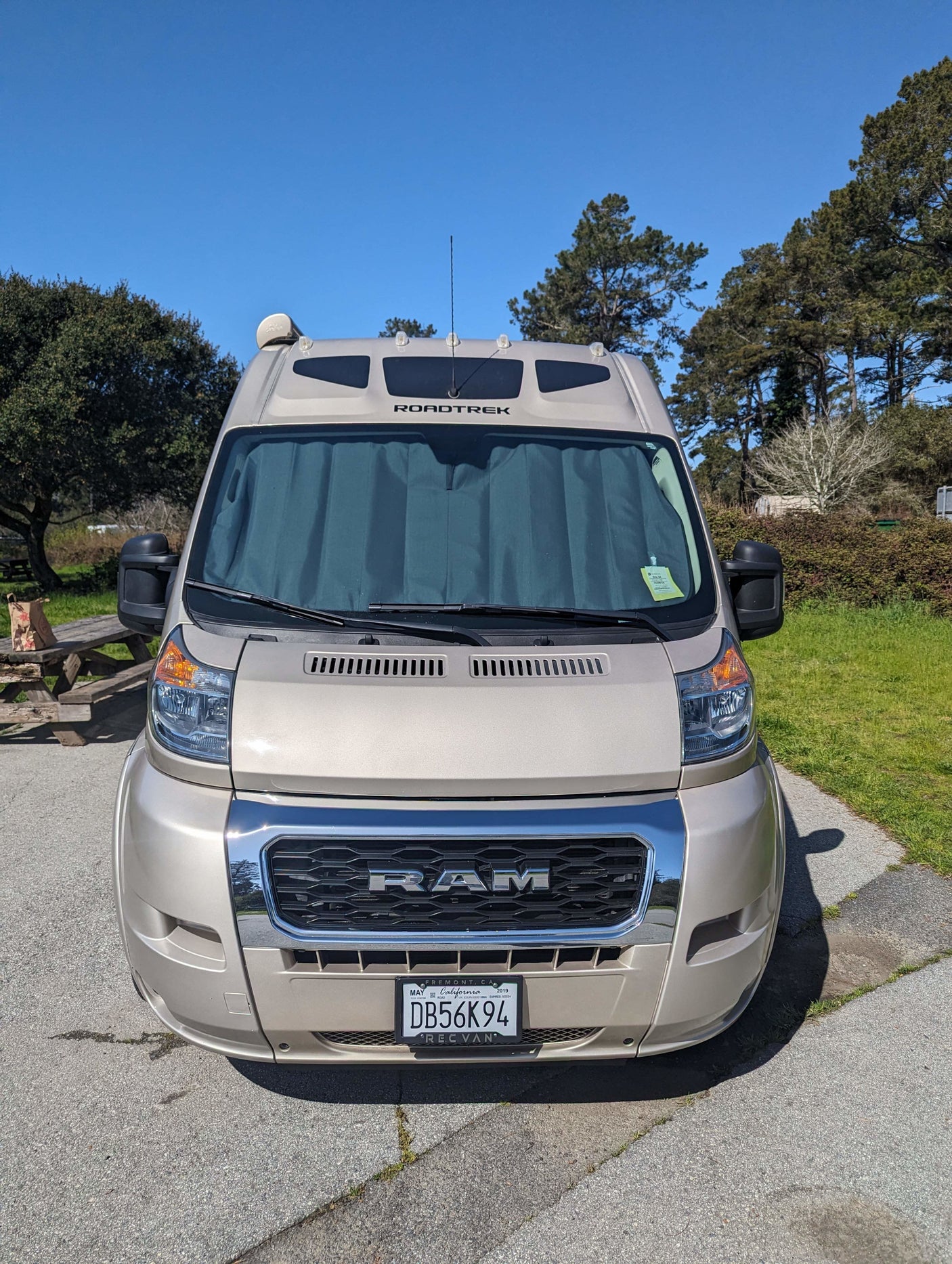 Front view of a tan Ram ProMaster Roadtrek campervan, ready for an RV rental adventure at a sunny campsite.
