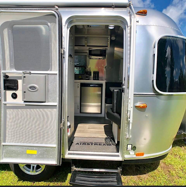 Step inside this Airstream travel trailer RV rental. Its open door reveals a compact kitchen with a fridge & microwave.