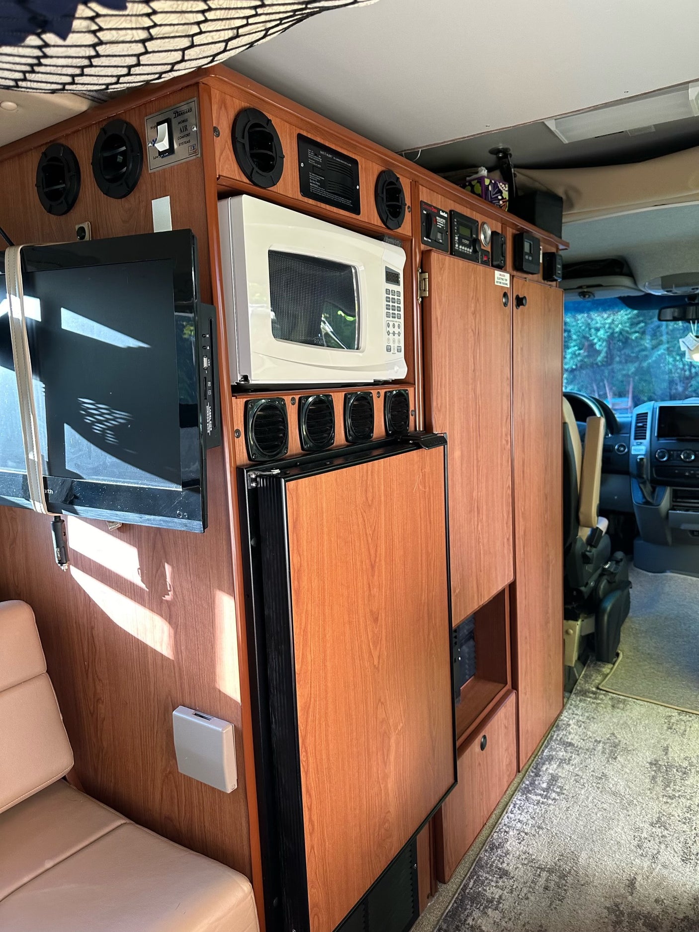 RV rental interior: wood cabinetry with TV, microwave, refrigerator, and control panel for mobile comfort.