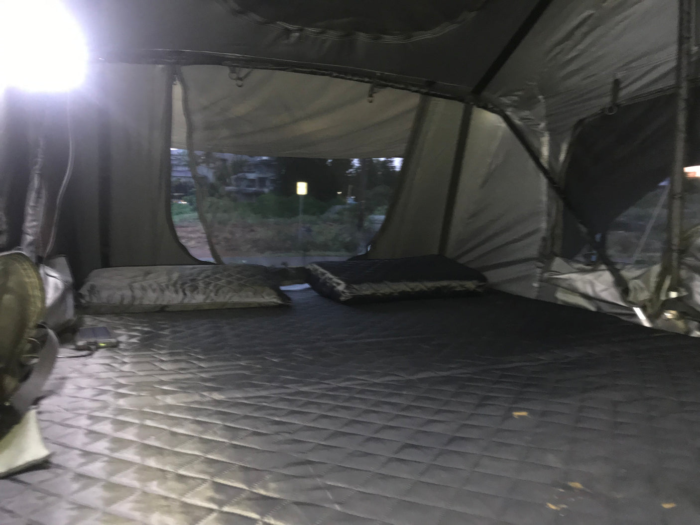 Comfortable RV rental rooftop tent interior with quilted bed & pillows, offering a night view for travel & camping.