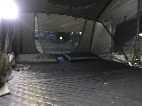 Comfortable RV rental rooftop tent interior with quilted bed & pillows, offering a night view for travel & camping.