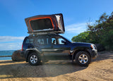 Experience beach camping with this RV rental alternative: a Nissan Xterra SUV with a deployed rooftop tent by the ocean.