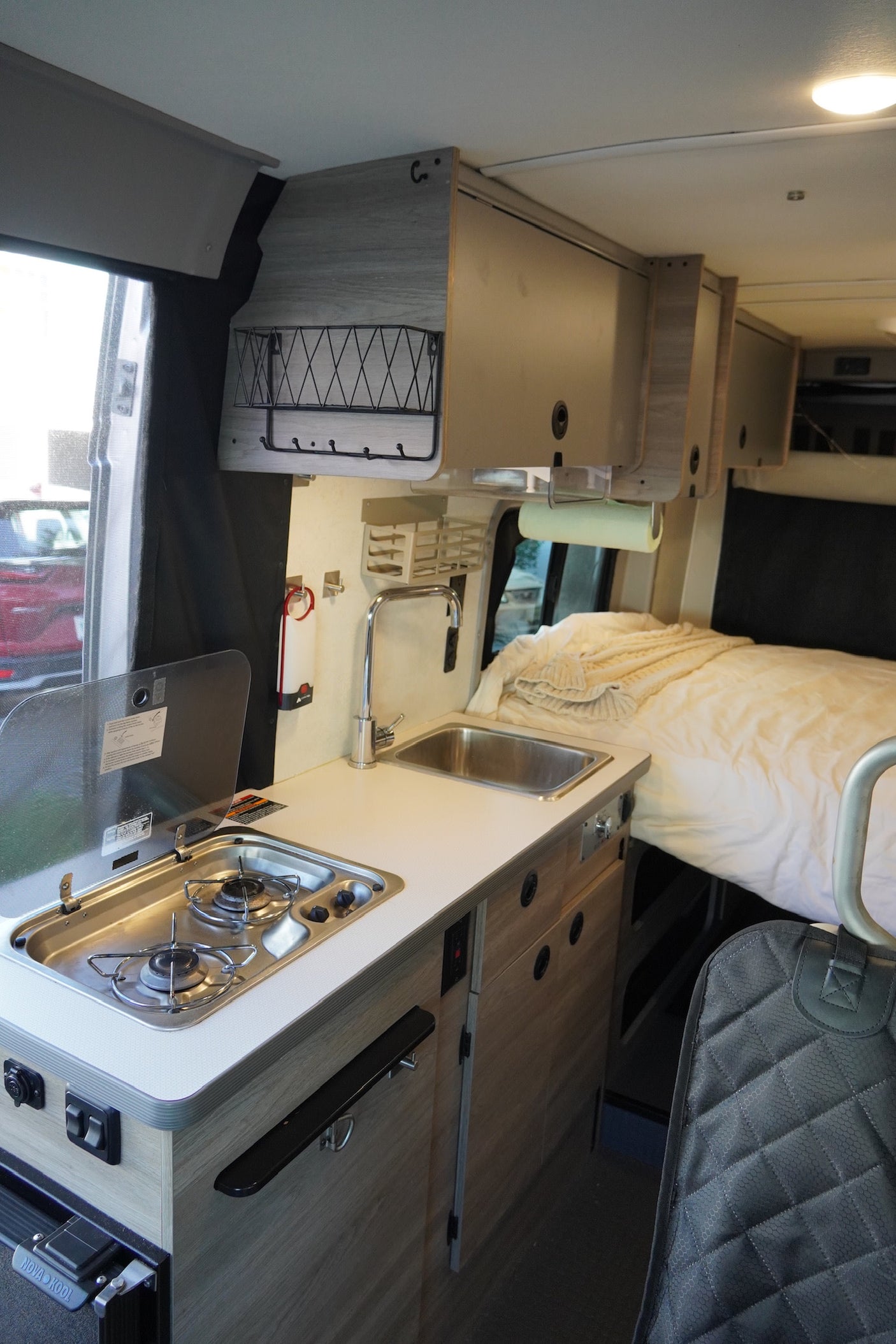 This RV rental's interior features a compact kitchen with a stove, sink, and overhead storage, leading to a comfortable bed.