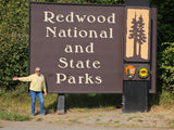 Happy traveler at Redwood National and State Parks sign, perfect for an RV rental adventure.