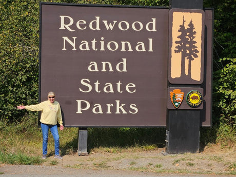 Happy traveler at Redwood National and State Parks sign, perfect for an RV rental adventure.