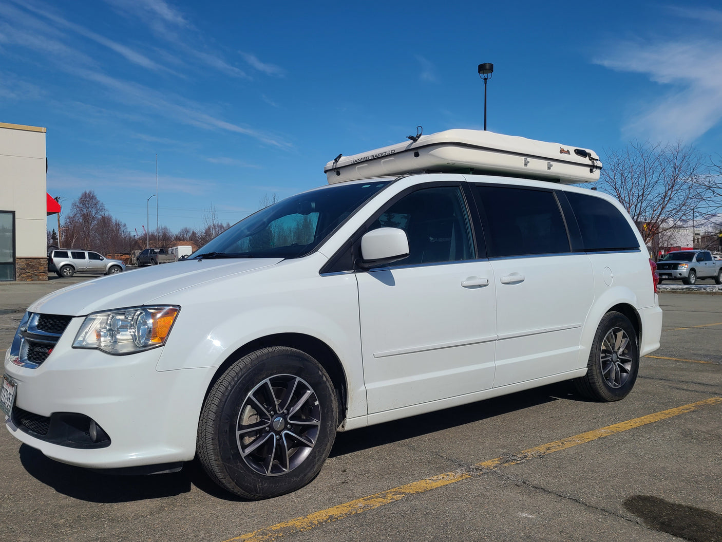 White Dodge Grand Caravan with a James Baroud rooftop tent, parked. Ideal RV rental setup for adventure.