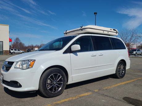 White Dodge Grand Caravan with a James Baroud rooftop tent, parked. Ideal RV rental setup for adventure.