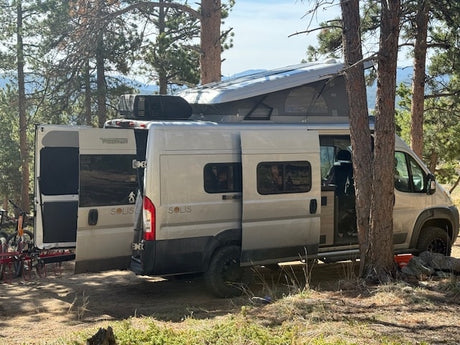 RV rental adventure: Two Winnebago Solis campervans, one with a pop-top, parked among trees with bikes.
