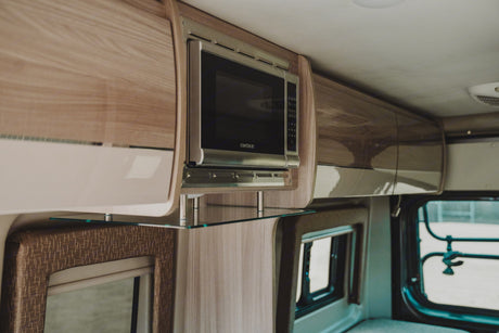 Inside an RV rental, a sleek Contoure microwave, wood cabinets, and glass shelf create a functional, compact kitchen space.