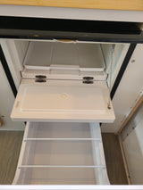 RV rental kitchen: opened compact refrigerator with white plastic shelves & lower pull-out storage drawer.