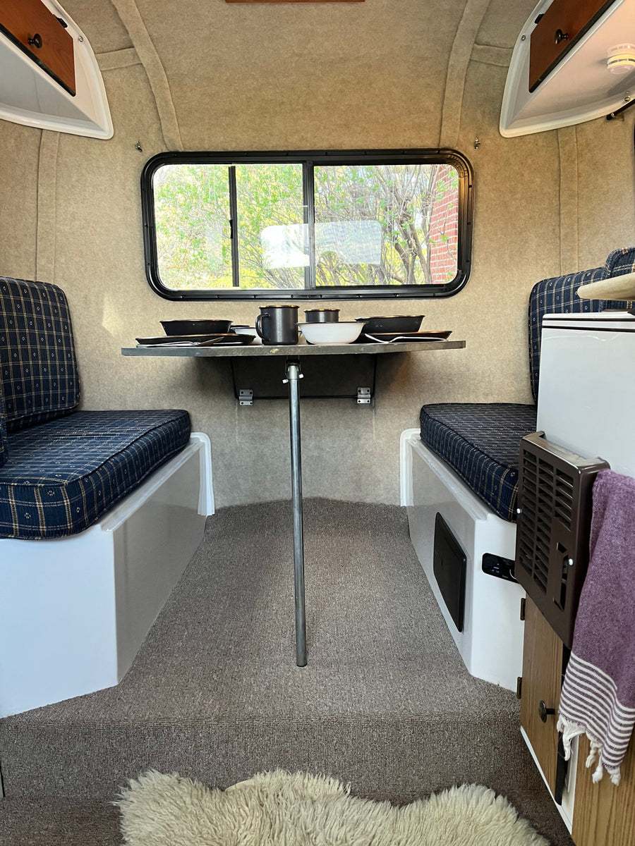 Compact RV rental interior: cozy dining area with plaid cushions, table, and window views.