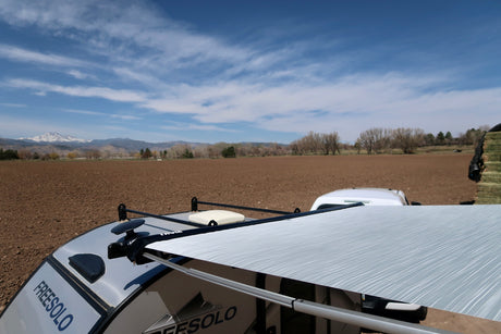 Freesolo RV rental: a trailer with an open awning overlooks a vast plowed field and distant snow-capped mountains.