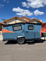 Blue Cricket travel trailer, a unique RV rental option, parked on asphalt. Ideal for outdoor adventures under clear skies.