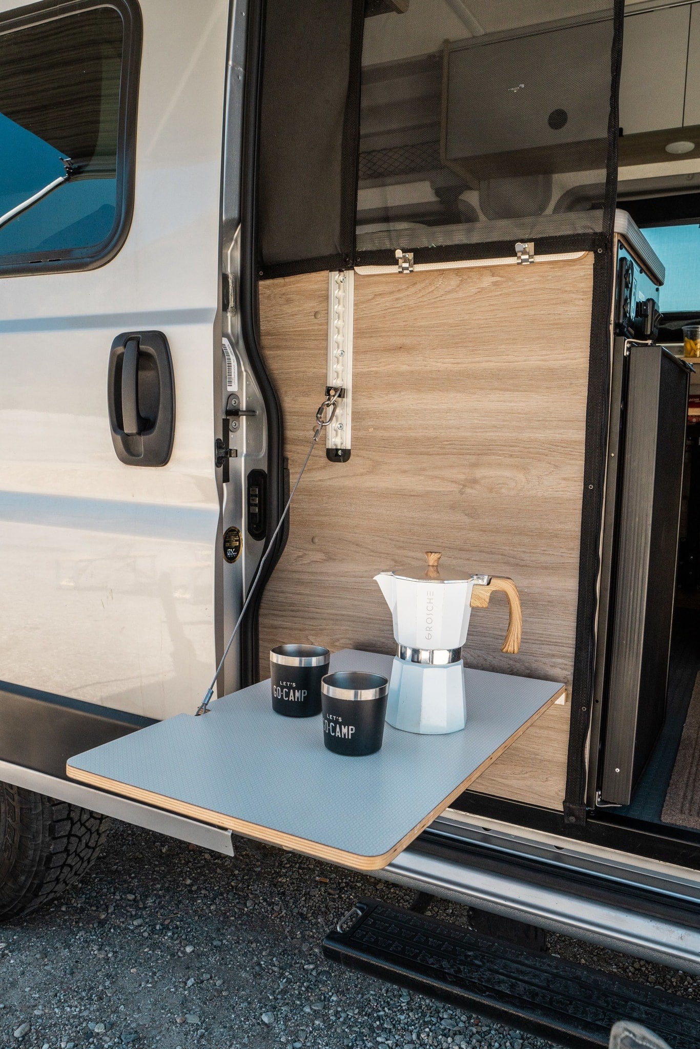 Mobile coffee station for your RV rental: a fold-down table with a white Moka pot and "LET'S GO-CAMP" mugs by the open van door. — photo 8