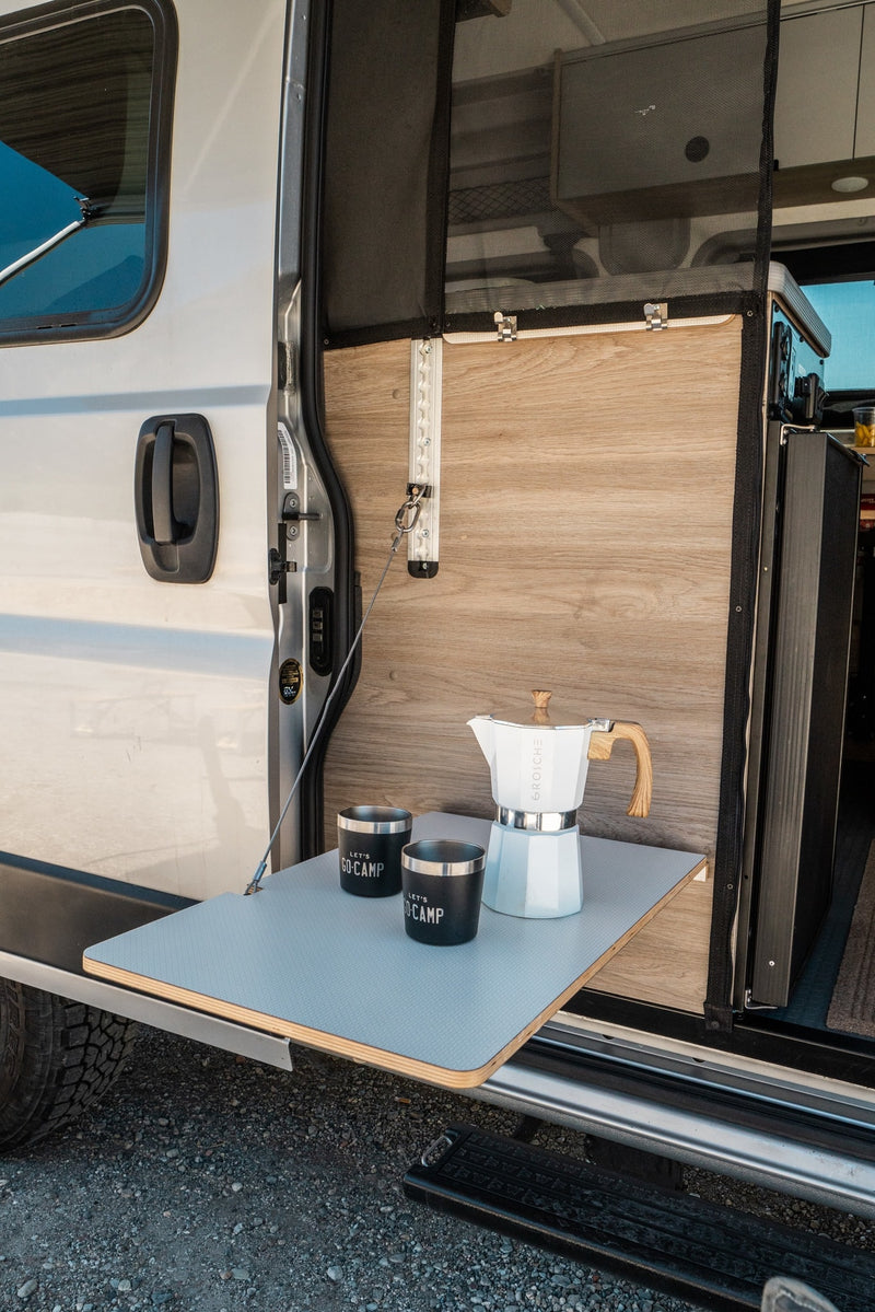 Mobile coffee station for your RV rental: a fold-down table with a white Moka pot and "LET'S GO-CAMP" mugs by the open van door. — photo 8