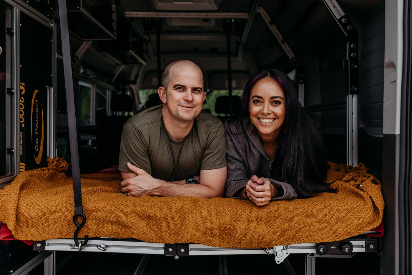 Smiling couple in their RV rental bed, ready for adventures. Interior shows custom features & a Go Power! inverter. — photo 16