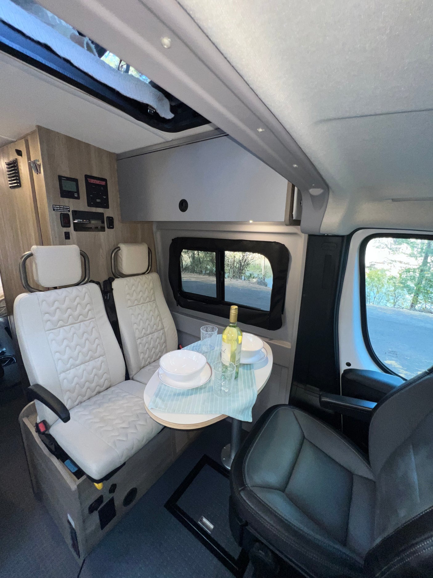 RV rental interior with a dining setup, light swivel seats, controls, and an outdoor view.