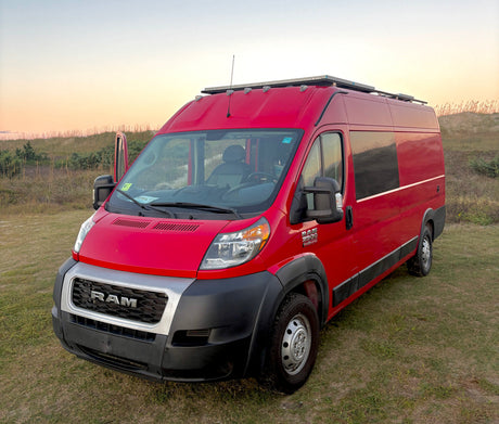 Red Ram ProMaster RV rental camper van, solar-equipped, parked on grassy dunes at golden hour for adventure travel.