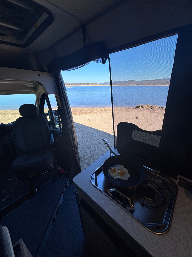 Breakfast with a view! Frying eggs on a stove inside an RV rental parked by a peaceful lake and sandy beach. — photo 11