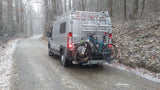 Gray RV rental van with mountain bikes on a snowy forest road. Ideal for winter adventures.