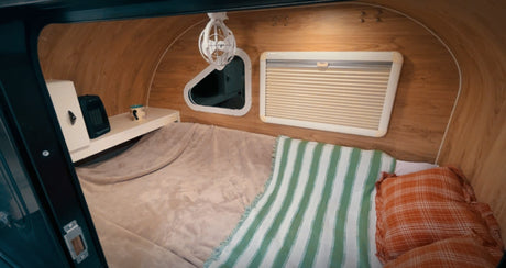 Compact rv rental interior showing a cozy sleeping area with wood paneling, a bed, heater, fan, and windows.