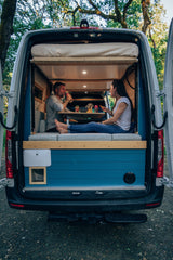 Couple enjoying a casual meal inside their cozy RV rental camper van, doors open to nature. Perfect for van life.
