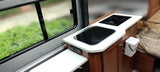 An RV rental's modern kitchenette setup: Includes an induction cooktop, sink, and a large window looking out to nature.