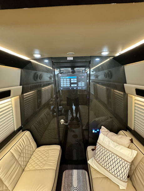 Inside a luxury RV rental: comfortable cream quilted seats, large central screen, glossy dark walls, and ambient lighting.