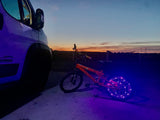 An RV rental with a glowing purple bike, parked at twilight with a vibrant sunset.