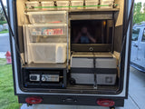 Organized RV rental rear compartment features an outdoor kitchen with a Blackstone griddle, portable cooler, and tiered storage bins.