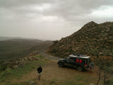 An overland truck camper on a dirt mountain road with a person walking. Perfect for rugged travel. Consider an RV rental adventure!