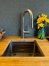 Sleek RV rental kitchen: bamboo counter, stainless sink with pull-down faucet, dark textured backsplash, and yellow flowers.