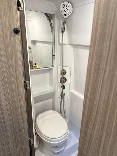 Experience the compact convenience of this RV rental's bathroom, featuring a white toilet, mirror, and handheld shower with controls.