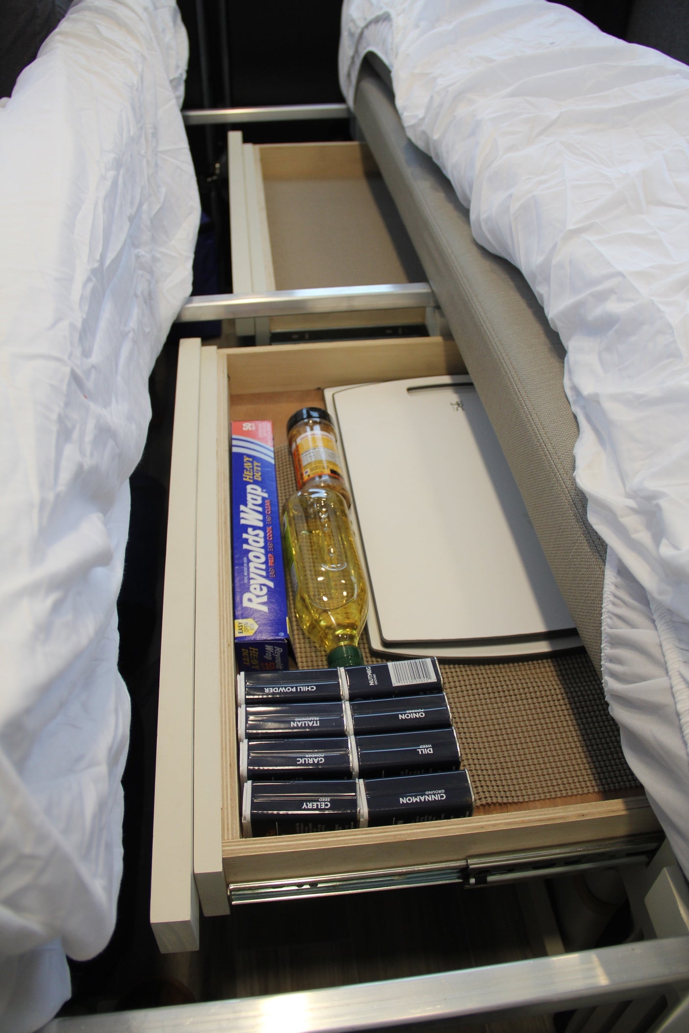 Compact kitchen supplies: foil, oil, cutting board, and spices neatly organized in an RV rental under-bed drawer.