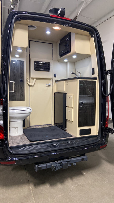 Luxury RV rental van interior: a compact bathroom with toilet, full kitchenette with sink, microwave, and refrigerator.